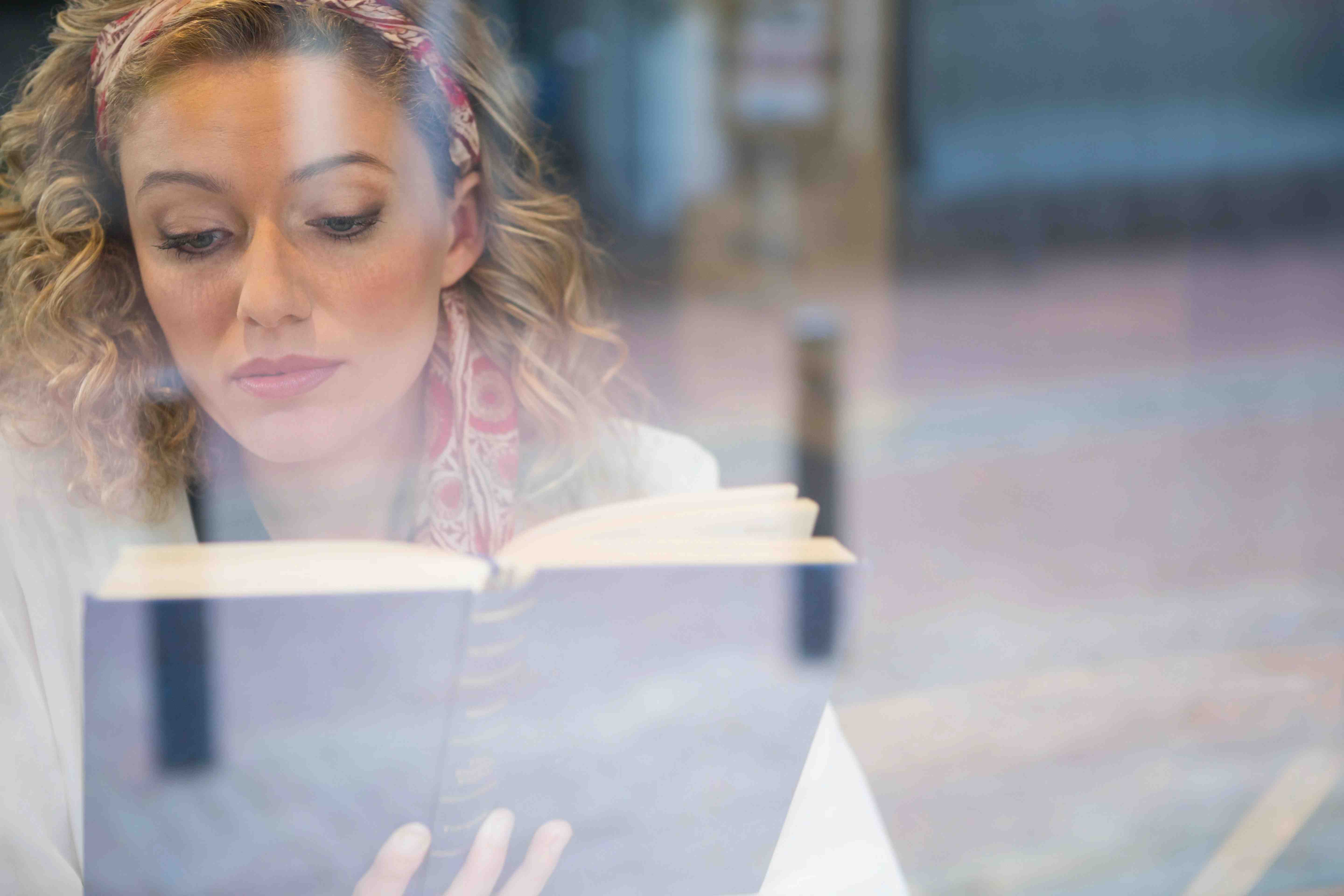 beautiful-woman-reading-book-seen-through-cafe-FACLPYX-min