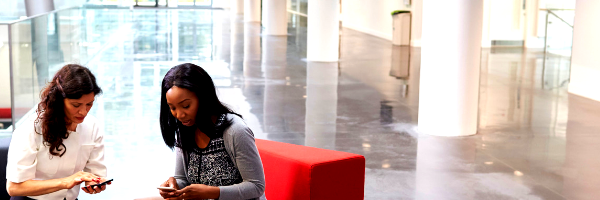 two-businesswomen-using-mobile-phones-in-lobby-of-P95QCDL-1