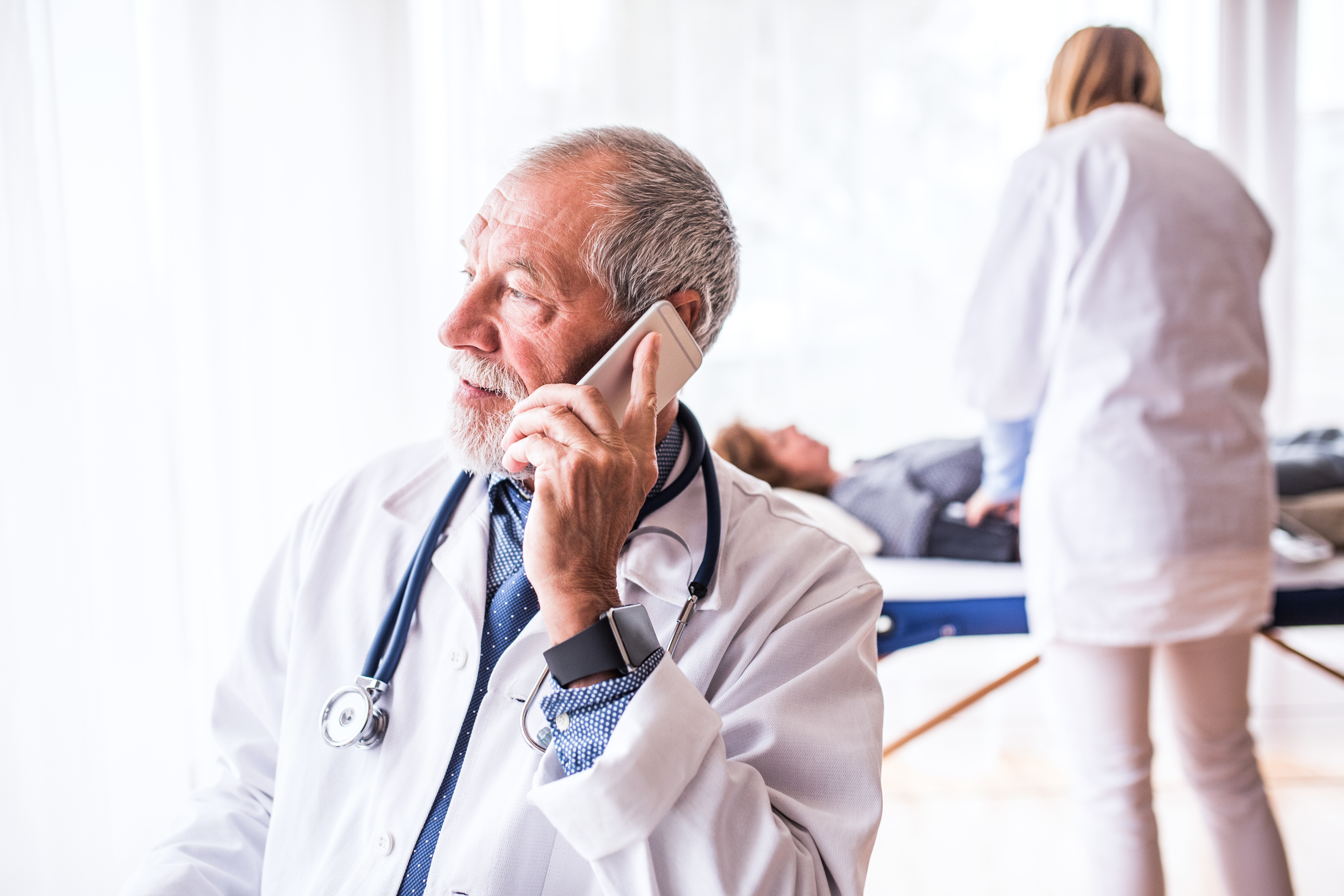 senior-doctor-with-smartphone-in-his-office-P3A8S6Z